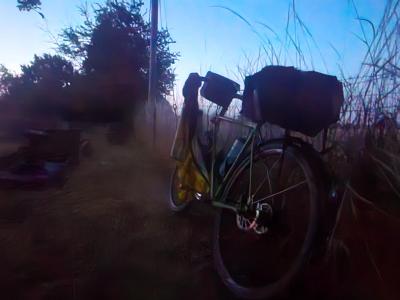 Sleep stop, Tadmarton Touring bicycle with black front and rear carriers, yellow jerkin hanging nearby, parked outdoors at dawn in misty graveyard with a field of tall grass framing the right side.