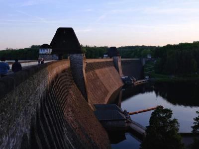 Large stone dam curving above a reservoir with water and forest below.