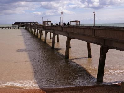Long concrete pier stretching into the sea with people walking beneath a cloudy sky.