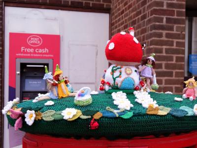 Knitted fairy-tale Easter scene with toadstool house and figures on top of a red postbox.