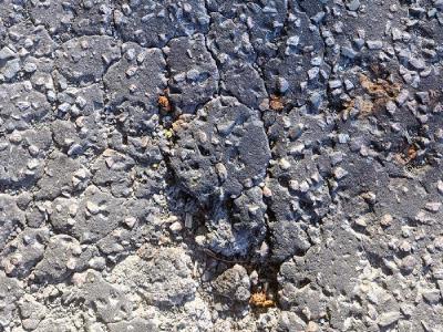 Close-up of deteriorated asphalt showing deep cracking with exposed aggregate and loose stones scattered across the broken surface.